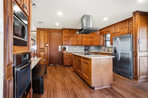 a kitchen with stainless steel appliances granite countertop a refrigerator a sink dishwasher a stove and a dining table with wooden floor