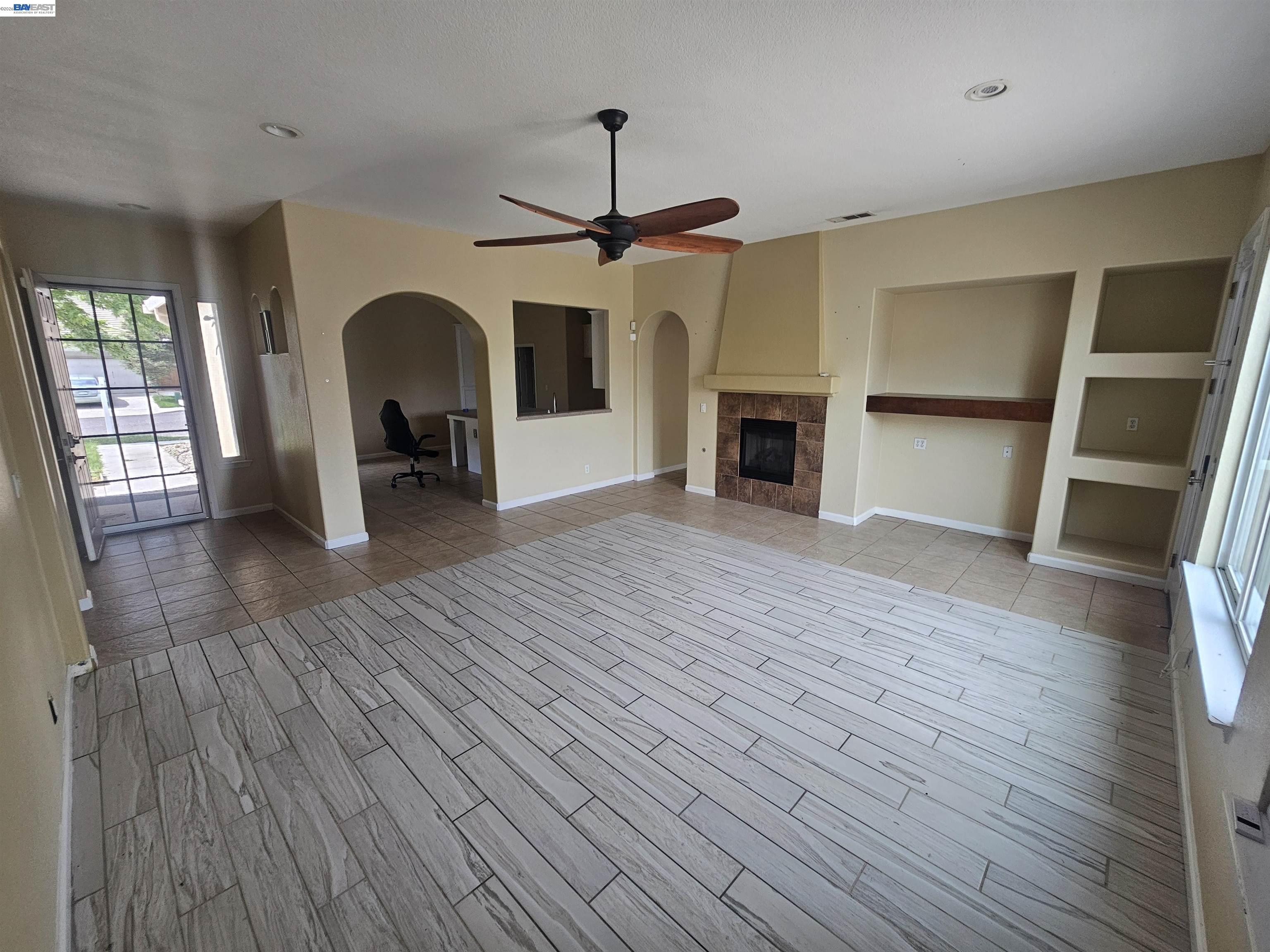 537 Bonanza Drive Newman, CA 95360 - Photo 2 of 16 an empty room with wooden floor a ceiling fan a fireplace and windows