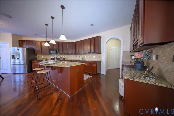 a kitchen with stainless steel appliances granite countertop a refrigerator a sink dishwasher a stove and white cabinets with wooden floor