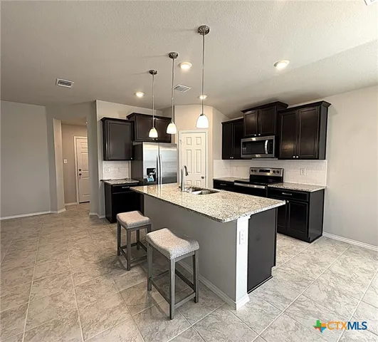 a large kitchen with stainless steel appliances kitchen island granite countertop a stove top oven a sink a counter top space and cabinets