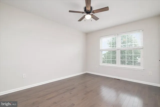 an empty room with wooden floor fan and windows