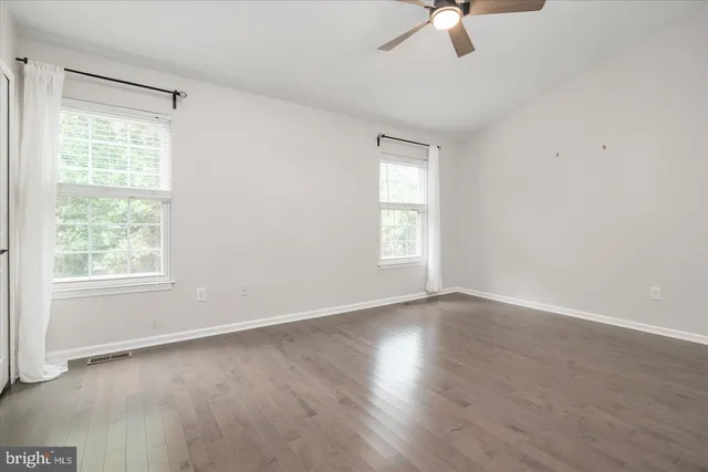 an empty room with wooden floor fan and windows