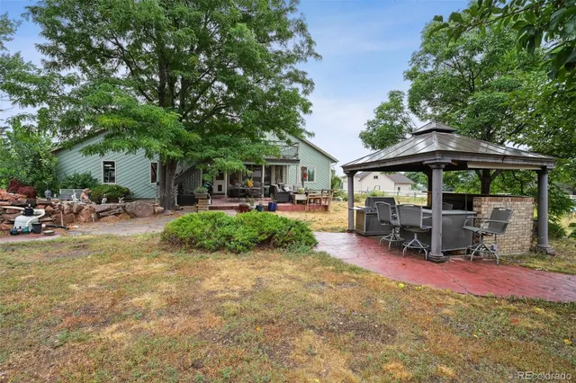 a view of a patio with table and chairs under an umbrella with large trees