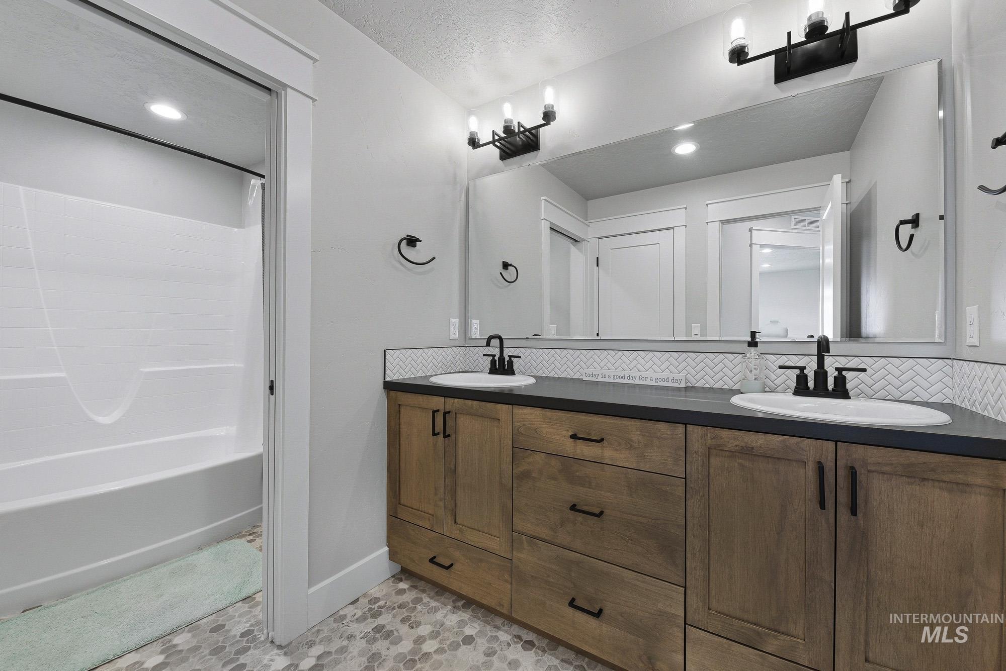 5676 East Zaffre Ridge Street Boise, ID 83716 - Photo 41 of 50 Bathroom featuring a double vanity with wood-finish cabinetry, black countertops, and a white herringbone tile backsplash