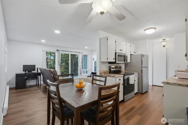 a kitchen with stainless steel appliances granite countertop a stove a refrigerator a kitchen island a dining table and chairs with wooden floor