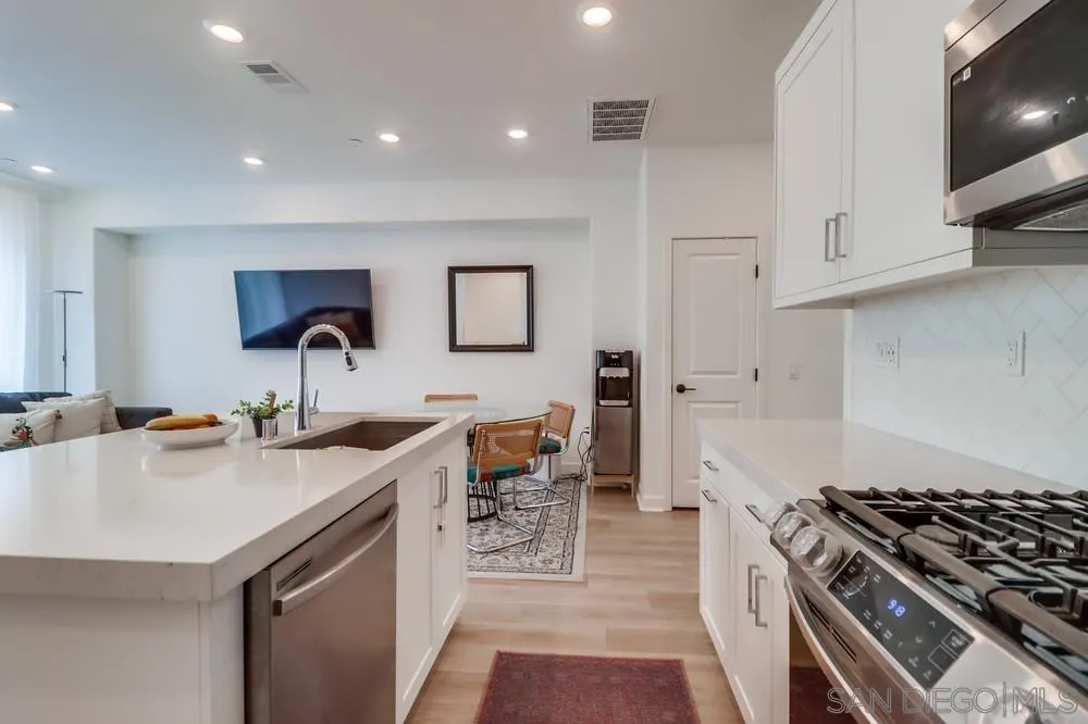 2408 Cascalote Loop San Diego, CA 92154 - Photo 16 of 50 a kitchen with stainless steel appliances a white stove top oven a sink a dining table and chairs with wooden floor