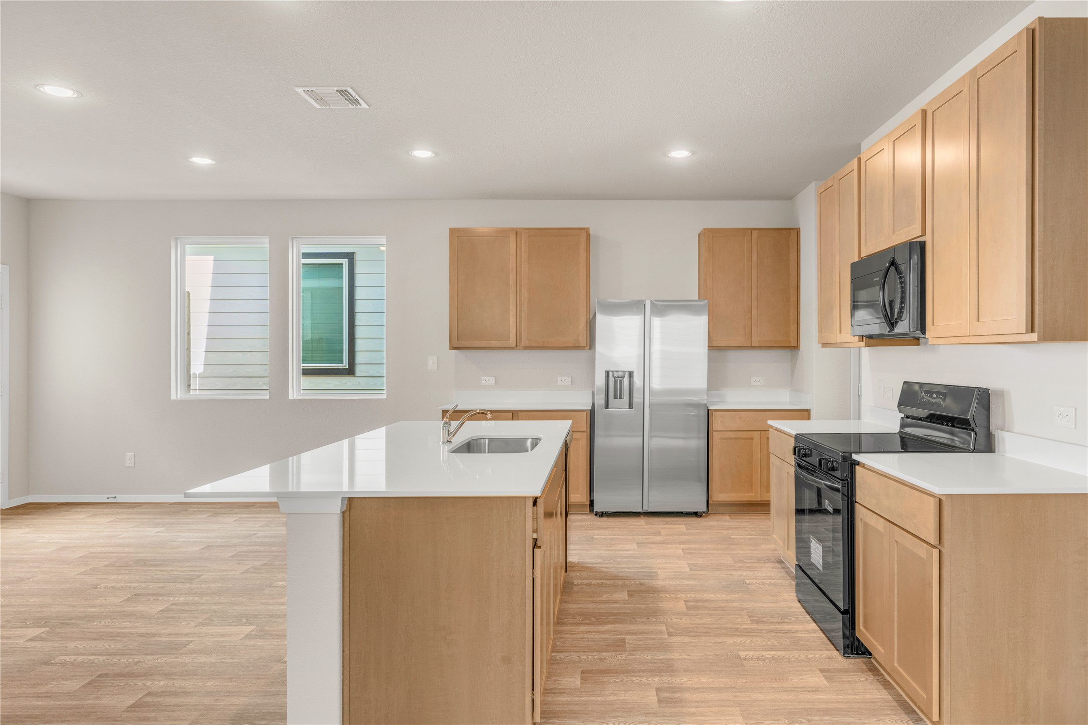 2615 Towy Road Manor, TX 78653 - Photo 9 of 38 Kitchen featuring black appliances, a center island with sink, light wood finished floors, recessed lighting, and light stone countertops