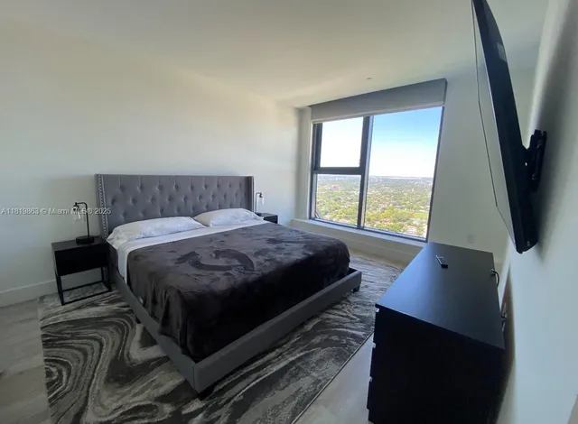 a bedroom with a bed a flat screen tv and a large window