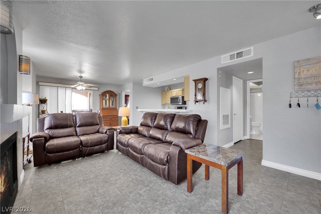 7570 West Flamingo Road, Unit 115 Las Vegas, NV 89147 - Photo 2 of 34 An inviting living room features a cozy fireplace and durable tile flooring, flowing seamlessly into the adjacent kitchen area.