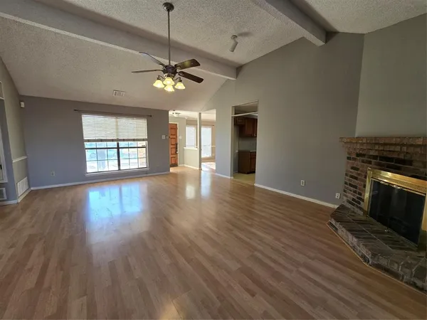 a view of an empty room with wooden floor fireplace and a window