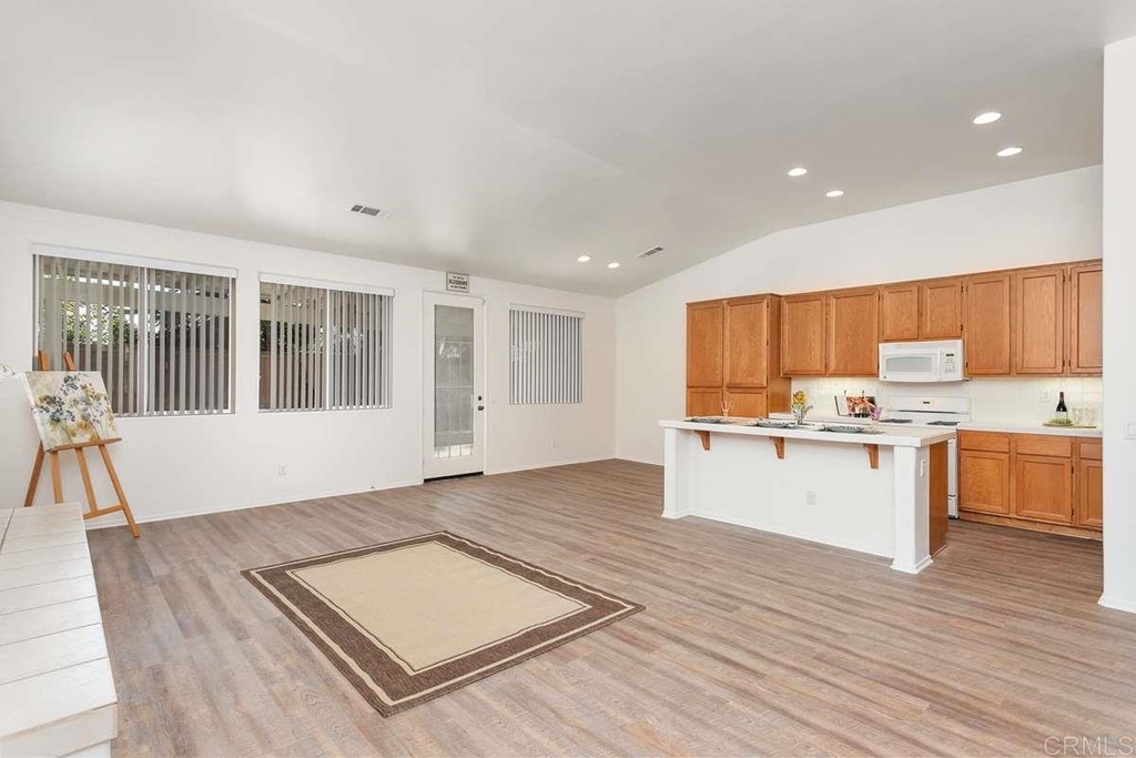 567 Big Sky Drive Oceanside, CA 92058 - Photo 7 of 27 a large white kitchen with kitchen island a stove a sink dishwasher and white cabinets with wooden floor
