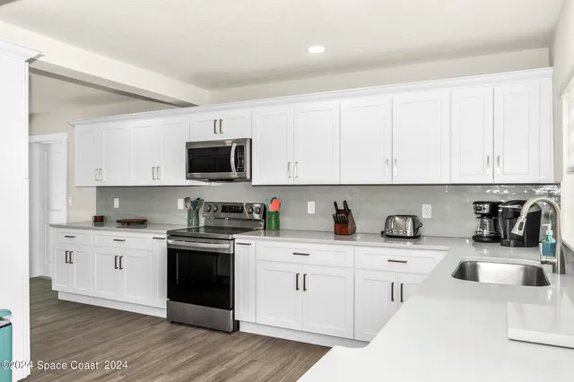 a kitchen with stainless steel appliances granite countertop a sink dishwasher a stove top oven a refrigerator with white cabinets and wooden floor