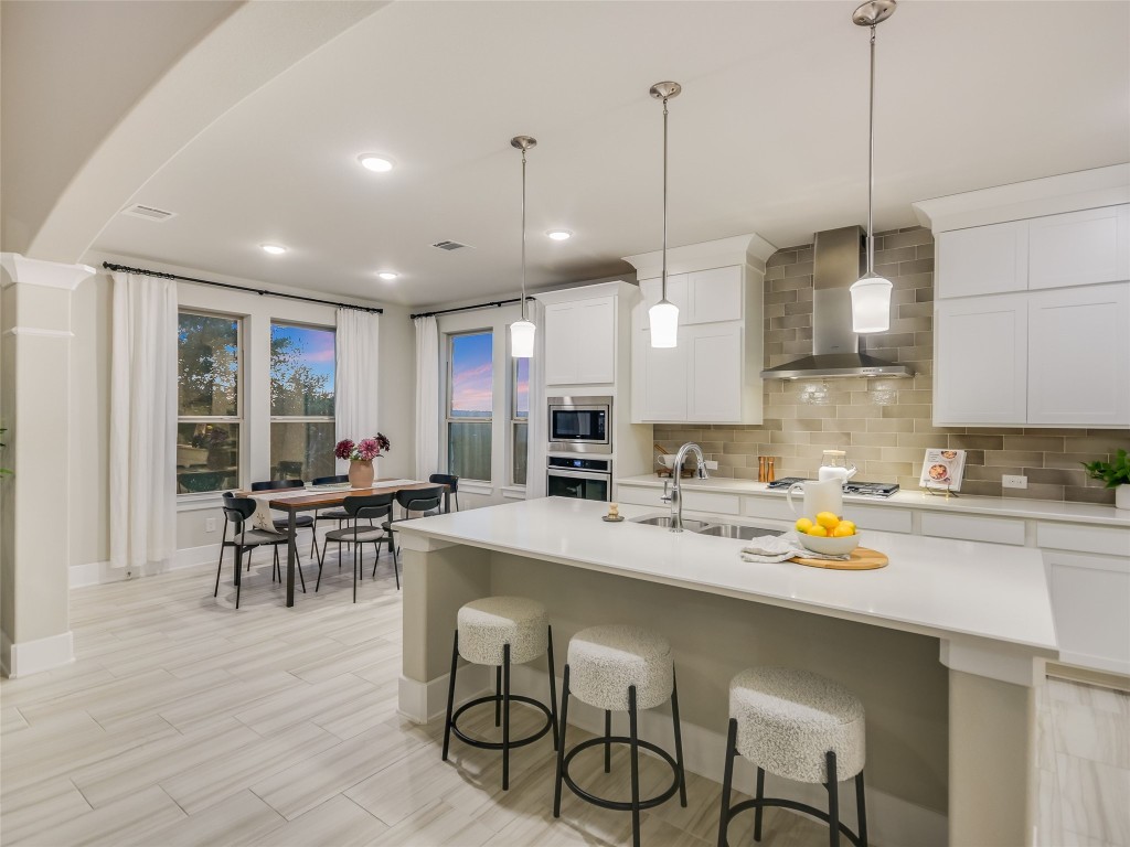 2610 Sunset Vista Circle, Unit 16 Spicewood, TX 78669 - Photo 14 of 28 Kitchen with wall chimney exhaust hood, decorative light fixtures, decorative backsplash, a breakfast bar area, and white cabinets