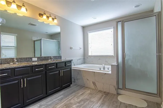 a spacious bathroom with a granite countertop double vanity sink a mirror and a bathtub