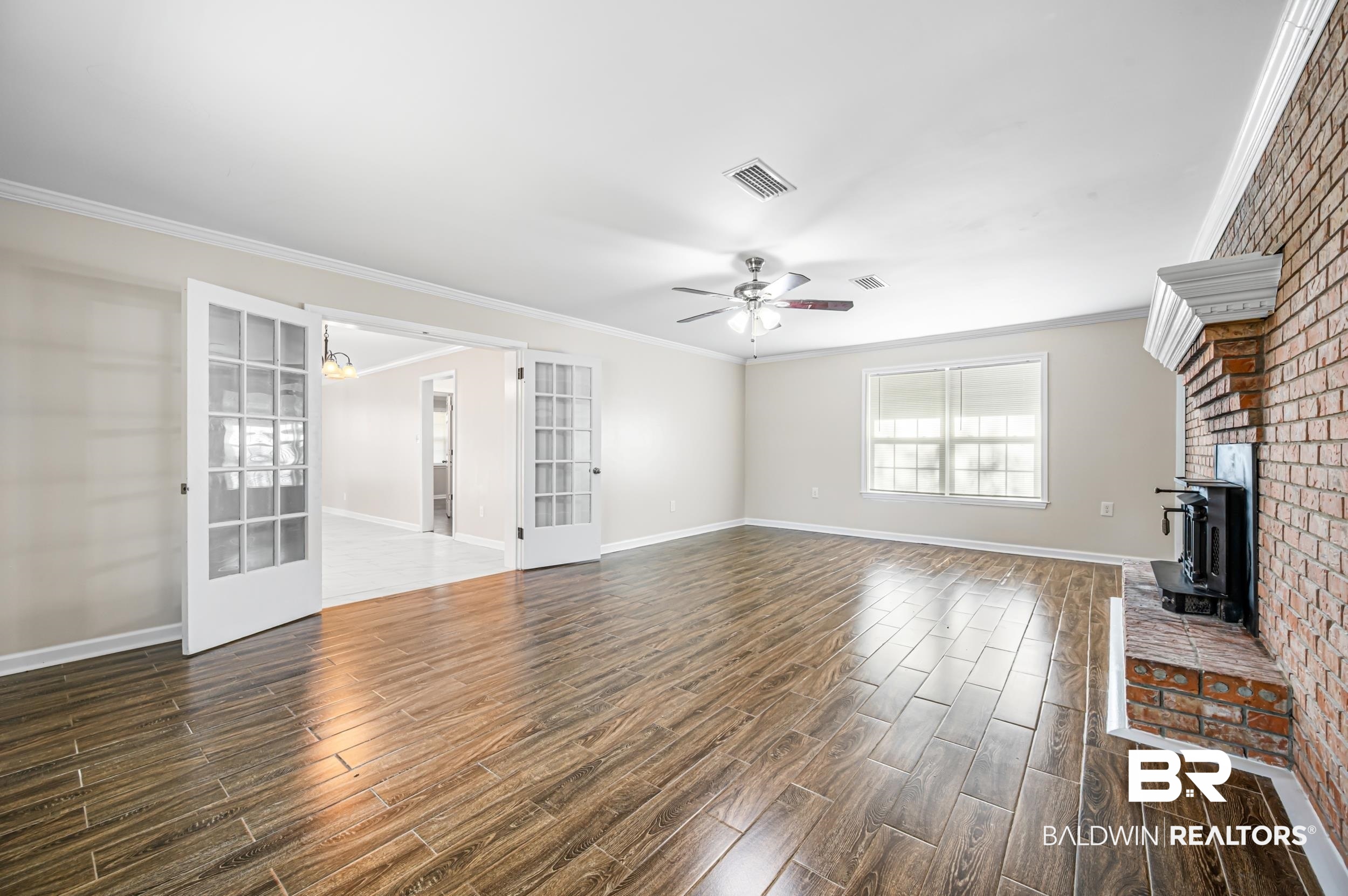 1605 Collier Avenue Bay Minette, AL 36507 - Photo 11 of 36 Unfurnished living room with ornamental molding, wood finish floors, a wood stove, a ceiling fan, and french doors