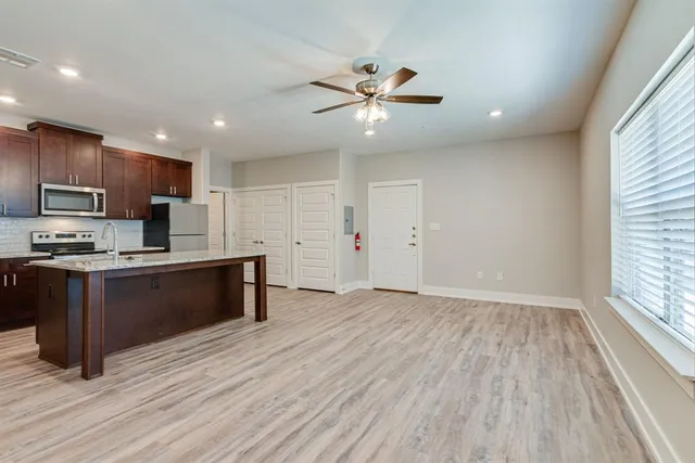 a kitchen with stainless steel appliances granite countertop a refrigerator a sink dishwasher a stove and a microwave oven on the wooden floor