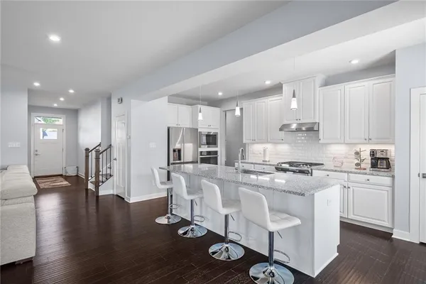 a kitchen with stainless steel appliances granite countertop a stove top oven a refrigerator a sink and white cabinets with wooden floor