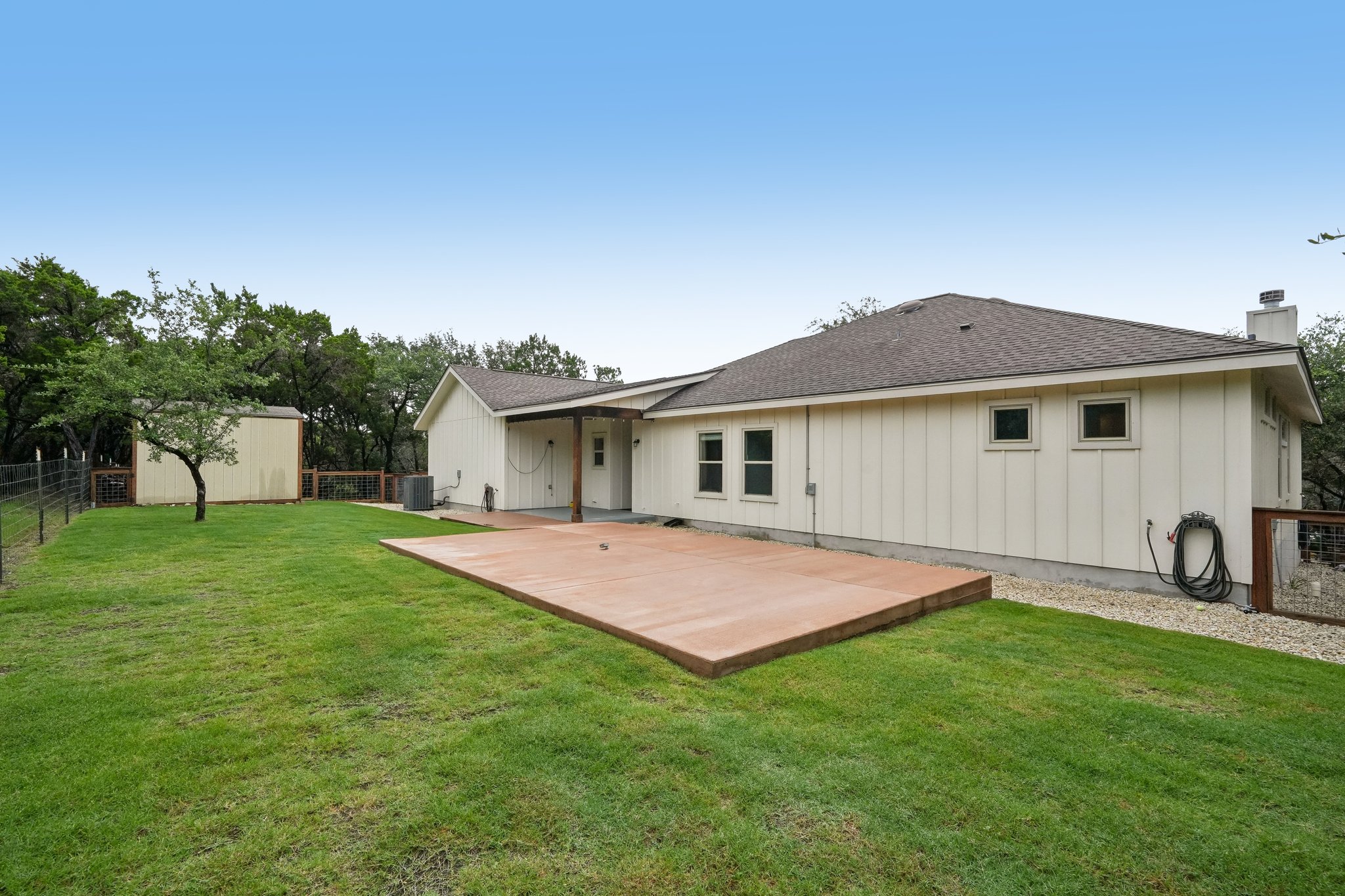190 Magnolia Meadow Spring Branch, TX 78070 - Photo 18 of 29 A verdant backyard with mature trees surrounds a cream-colored residence, featuring a sizable concrete patio for outdoor enjoyment.
