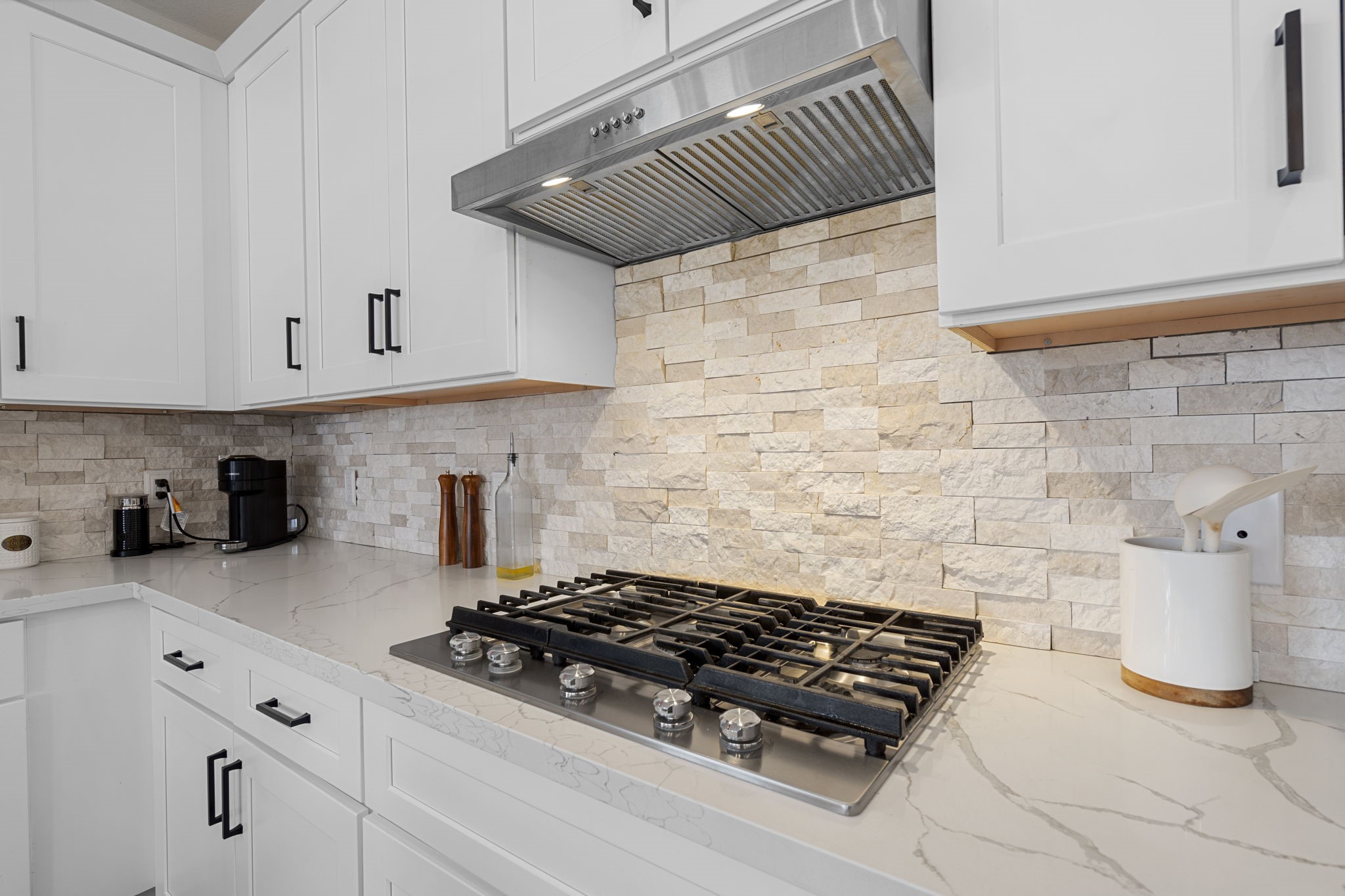 1294 County Road 5100 Cleveland, TX 77327 - Photo 8 of 27 A chef-inspired cooking space featuring a sleek gas cooktop, modern stainless steel vent hood, and elegant stone backsplash.