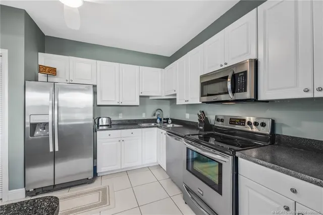 a kitchen with stainless steel appliances granite countertop a refrigerator a stove a sink and white cabinets