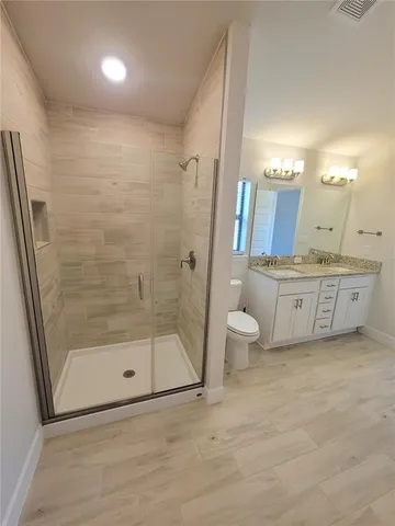 a bathroom with a granite countertop sink a toilet a mirror and shower