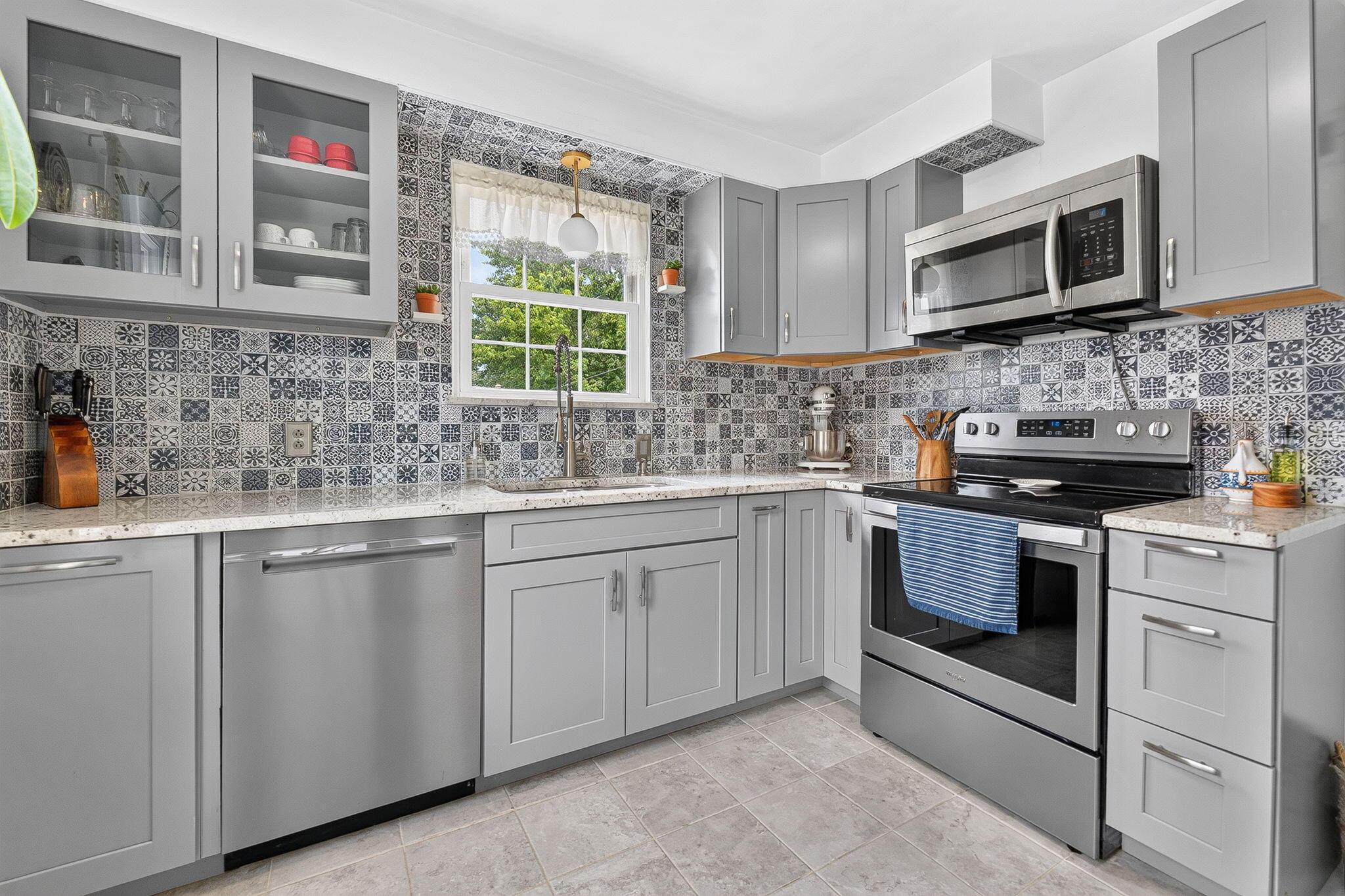492 Wetmore Road Columbus, OH 43214 - Photo 5 of 55 Kitchen featuring gray shaker-style cabinetry, a patterned tile backsplash, stainless steel appliances, light-toned countertops, and a single basin sink with a window above
