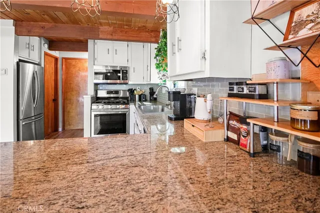 a kitchen with stainless steel appliances granite countertop a stove top oven a sink a refrigerator and white cabinets