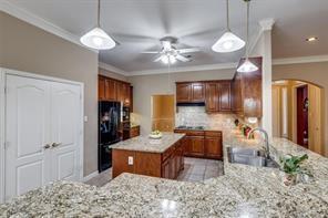 3036 Falcon Road Prosper, TX 75078 - Photo 19 of 20 Kitchen featuring granite countertops, wood cabinetry, a central island, stainless steel sink, and a ceiling fan with integrated lighting