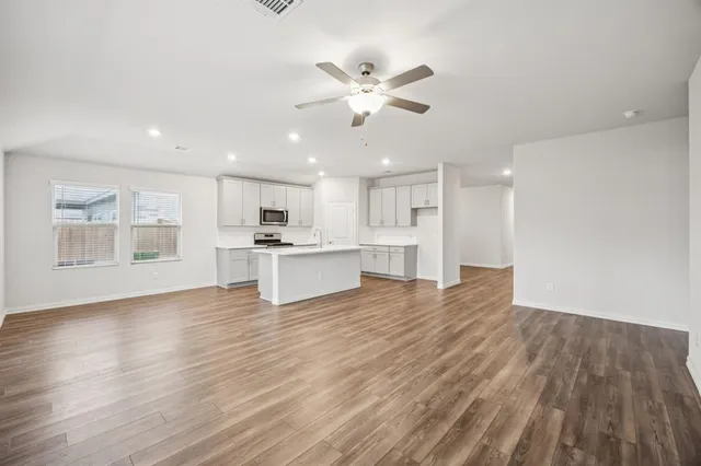 a view of an empty room with wooden floor and a kitchen