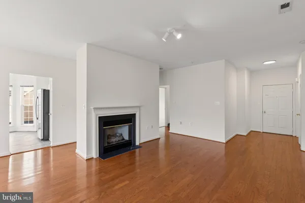 a view of an empty room with wooden floor fireplace and a window