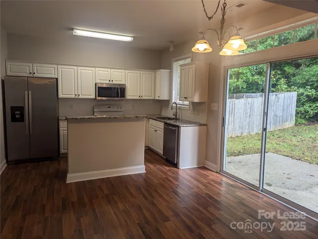 a kitchen with stainless steel appliances granite countertop a refrigerator a sink dishwasher a stove and white countertops with wooden floor