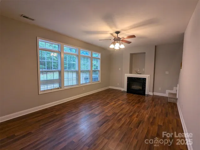 an empty room with wooden floor fan and windows