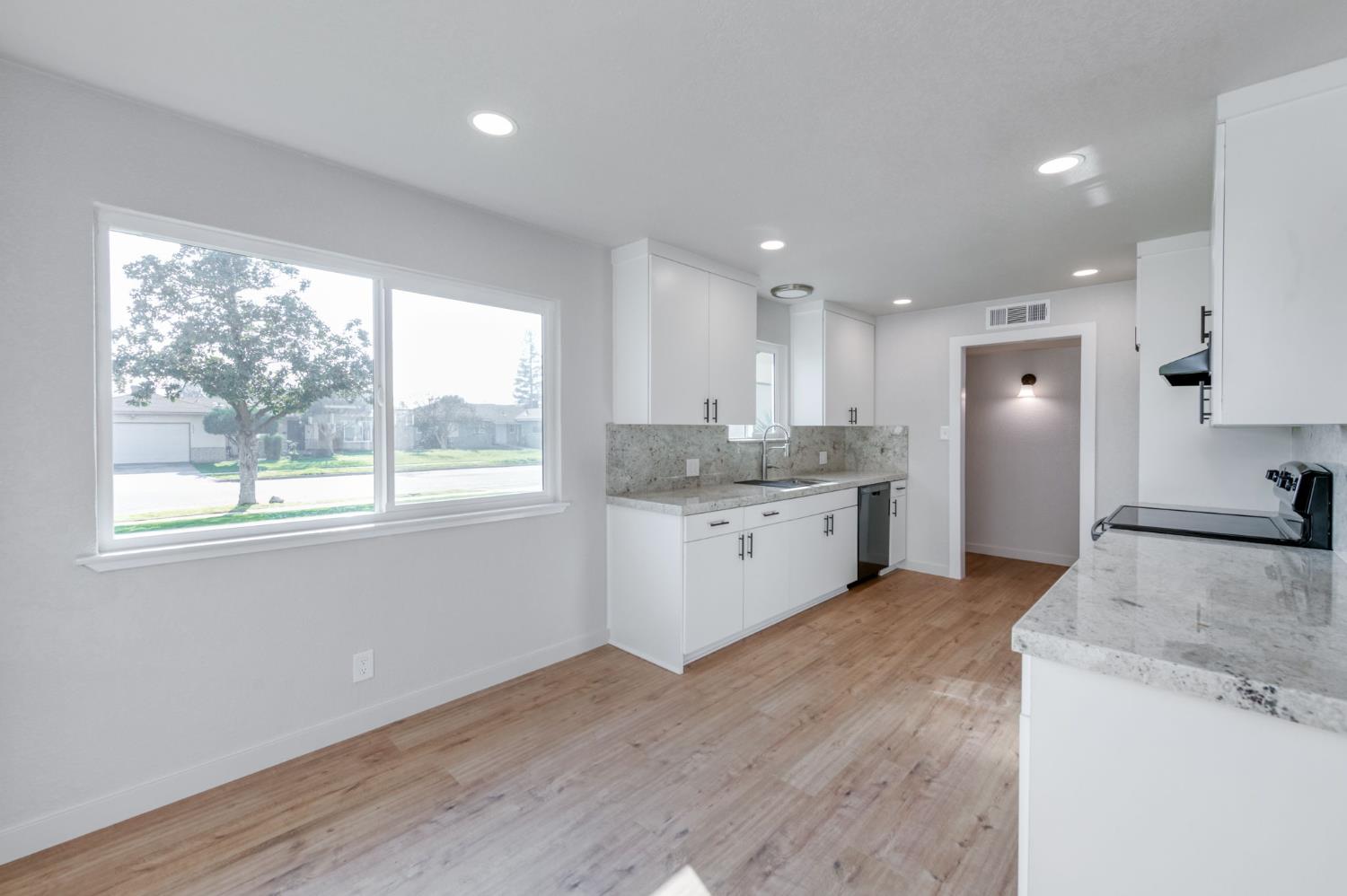 4031 East Pontiac Way Fresno, CA 93726 - Photo 14 of 46 a large kitchen with a stove a sink a refrigerator and white cabinets with wooden floor next to windows