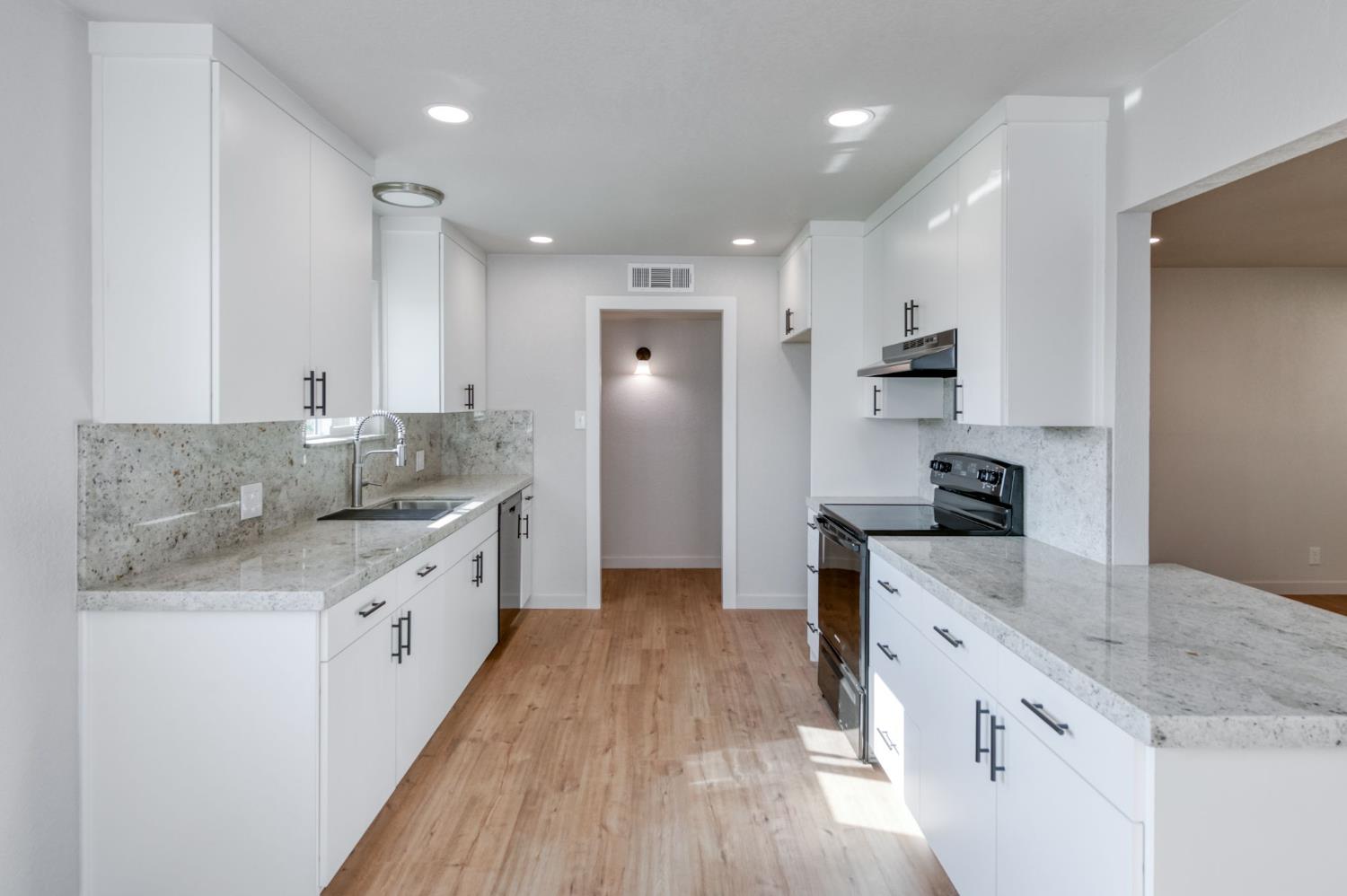 4031 East Pontiac Way Fresno, CA 93726 - Photo 16 of 46 a kitchen with granite countertop a sink stove refrigerator and white cabinets with wooden floor
