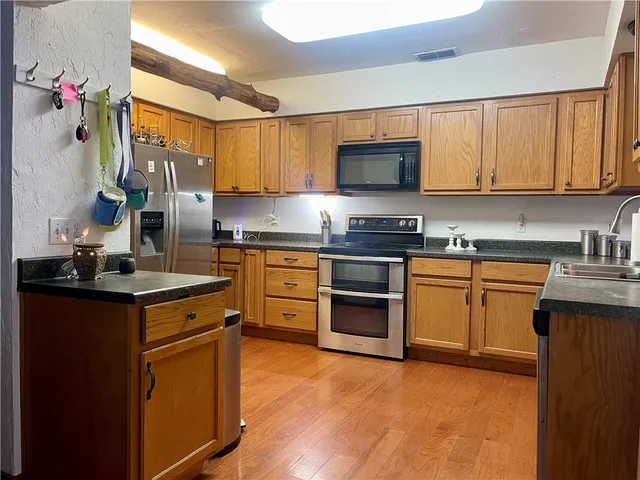 a kitchen with stainless steel appliances granite countertop a stove top oven a sink dishwasher and a refrigerator with wooden cabinets