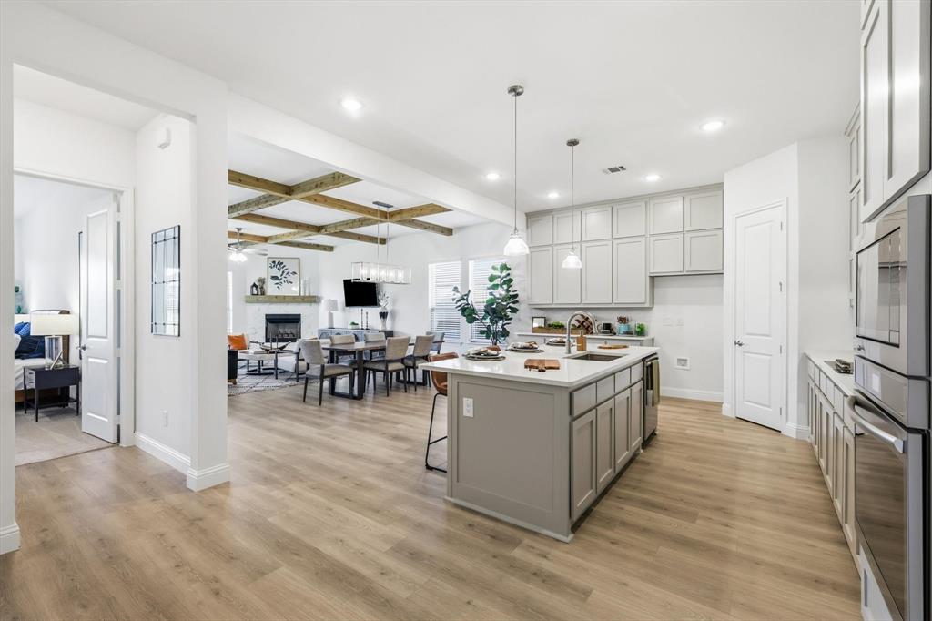 4017 Eagles Bluff Road Midlothian, TX 76065 - Photo 17 of 38 Open-concept living space featuring wood-finish flooring, a kitchen island with pendant lighting, light gray cabinetry, built-in stainless steel appliances, and a coffered ceiling with exposed wood beams