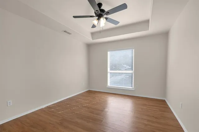 an empty room with wooden floor chandelier fan and windows