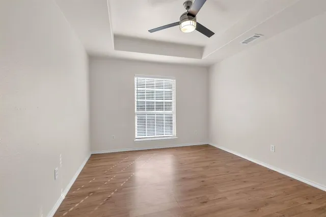 an empty room with wooden floor fan and windows