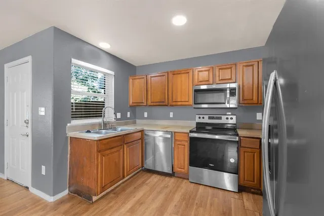 a kitchen with stainless steel appliances granite countertop a stove a sink dishwasher a refrigerator and a microwave oven with wooden floor