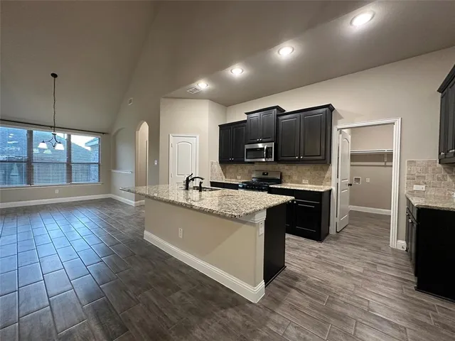 a large kitchen with granite countertop a stove a sink dishwasher a microwave oven and a dining table with wooden floor