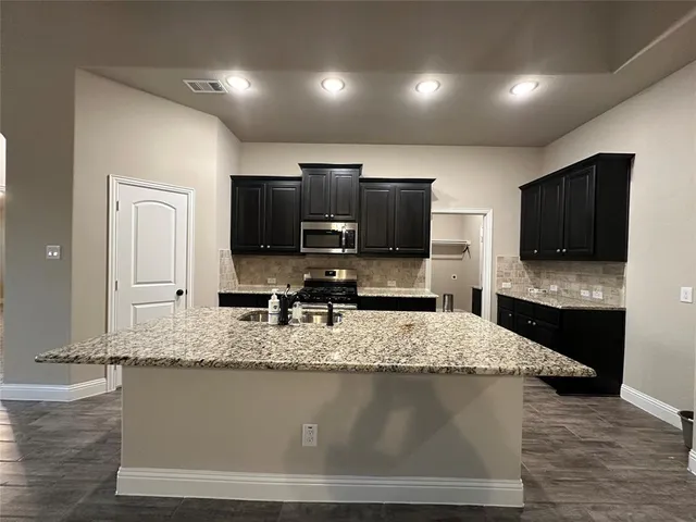 a large kitchen with granite countertop a stove a sink and a microwave