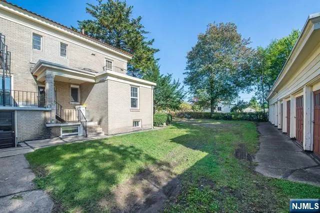 a view of a white house with a yard plants and large tree