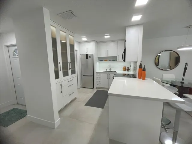 a large white kitchen with cabinets a sink a window and a refrigerator