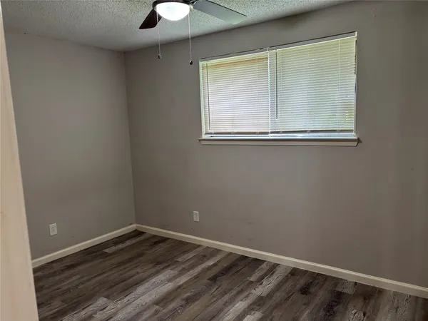 an empty room with wooden floor fan and windows