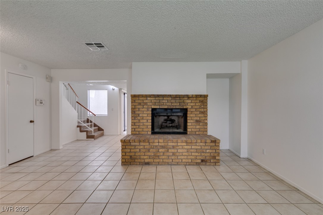 2681 Ruthe Duarte Avenue Las Vegas, NV 89121 - Photo 12 of 43 Unfurnished living room with a textured ceiling, visible vents, light tile patterned flooring, a brick fireplace, and stairs