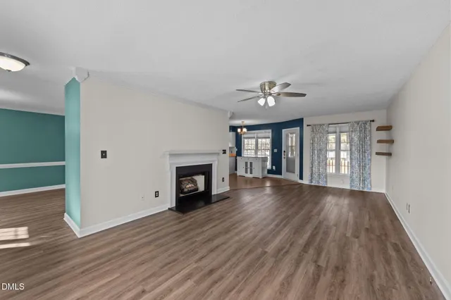 a view of an empty room with wooden floor fireplace and a window