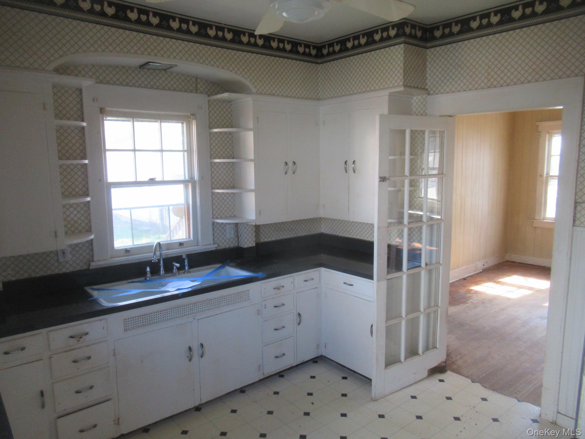 72 Waterstone Road Greenwood Lake, NY 10925 - Photo 6 of 20 Kitchen featuring white cabinetry with integrated shelving, dark countertops, a single basin sink with a chrome faucet, and patterned floor tiling