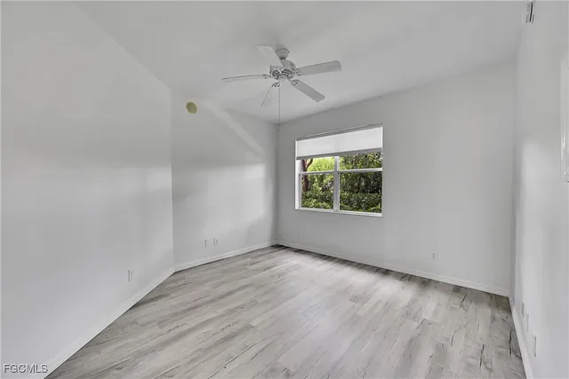 an empty room with wooden floor windows and fan