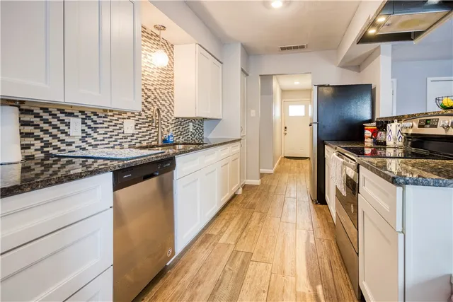 a kitchen with granite countertop a sink a counter top space stainless steel appliances and cabinets