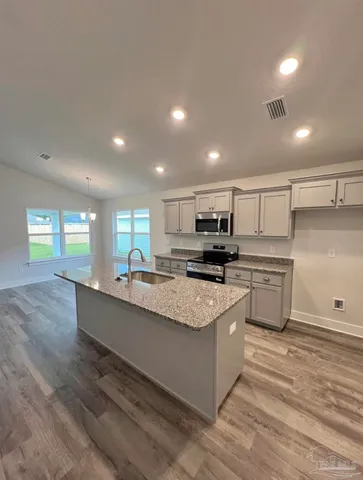 a large white kitchen with a stove a sink a refrigerator and white cabinets with wooden floor